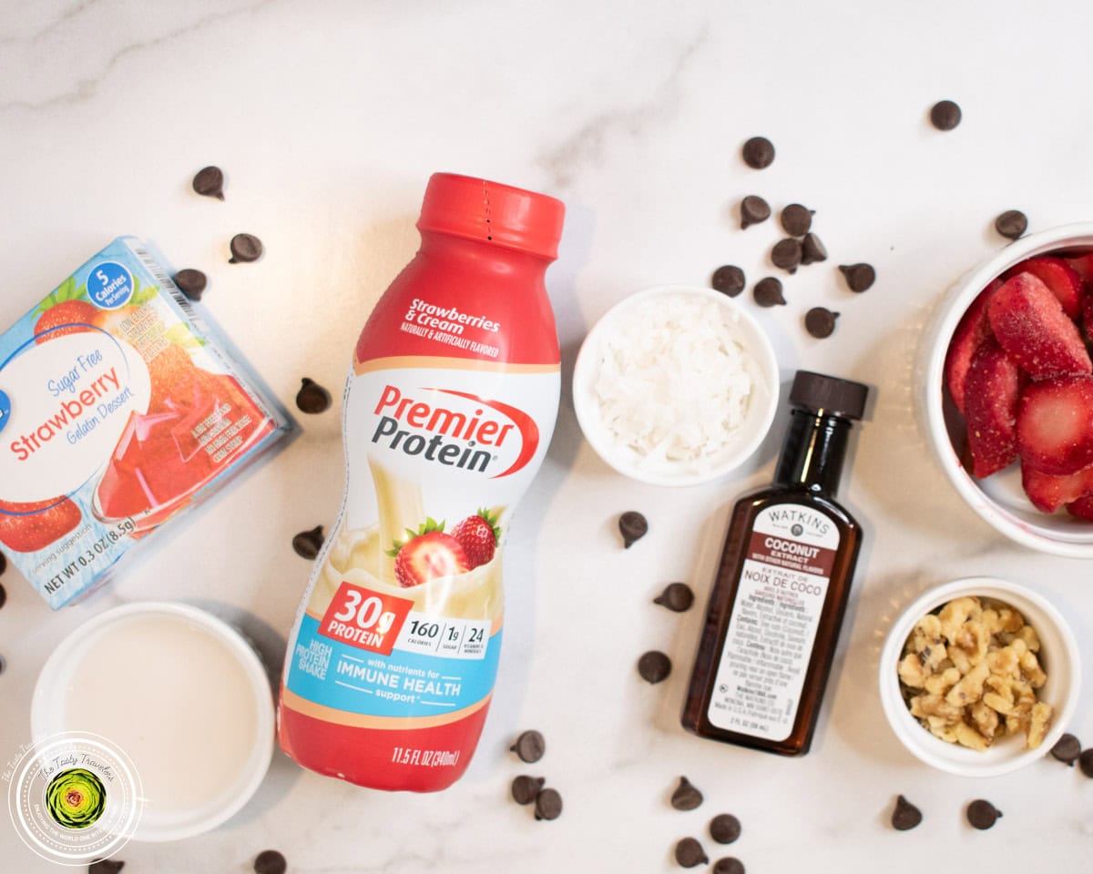 Ingredients for Ninja Creami strawberry coco-nut protein ice cream including strawberry protein shake, Jell-O mix, coconut extract, strawberries, walnuts, coconut, and chocolate chips