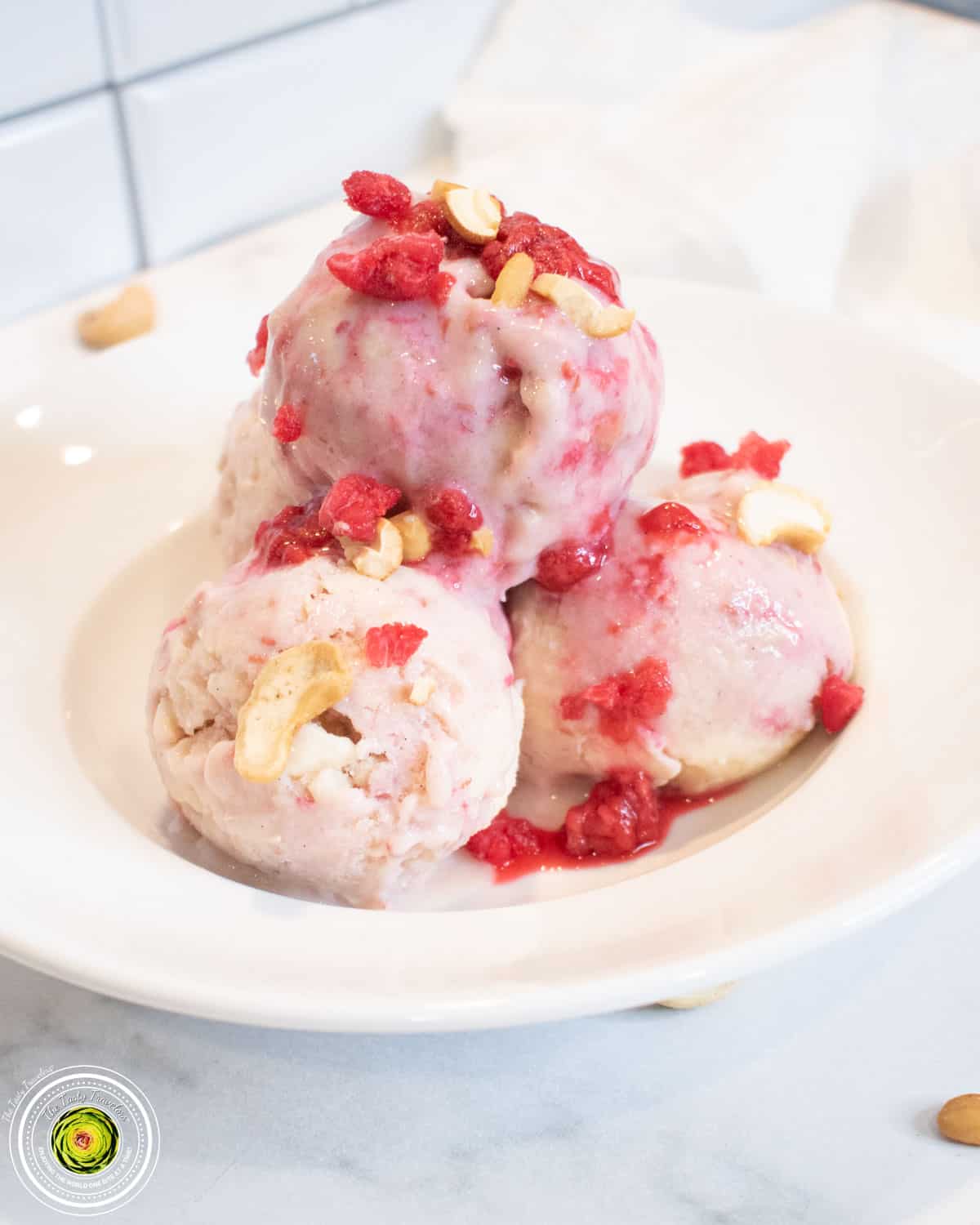 Homemade raspberry sauce being added to vanilla protein ice cream in a Ninja Creami container