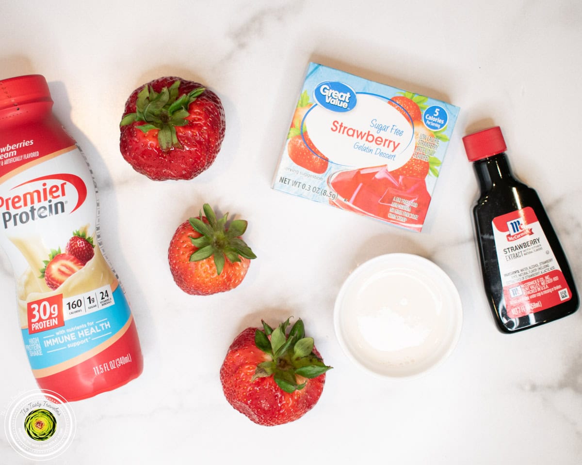 Ingredients for Ninja Creami super strawberry protein ice cream including strawberry protein shake, strawberry Jell-O mix, strawberry extract, and fresh strawberries