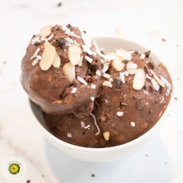 Almond Joy protein ice cream scoops in a white bowl, topped with sliced almonds and coconut flakes.