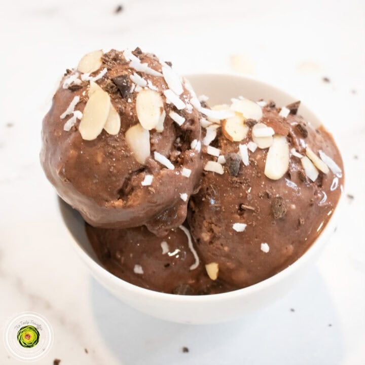 Almond Joy protein ice cream scoops in a white bowl, topped with sliced almonds and coconut flakes.