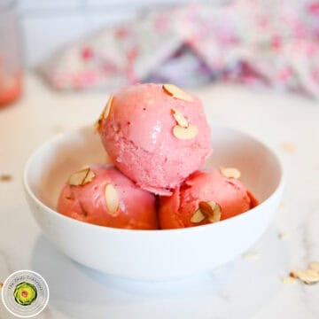 Delicious pink ice cream scoops with almond slices in a white bowl.