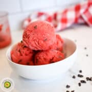 Vegan strawberry ice cream scoops in a white bowl on a white surface.