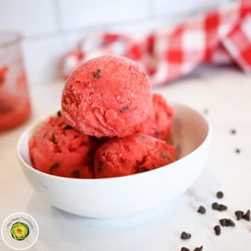 Vegan strawberry ice cream scoops in a white bowl on a white surface.