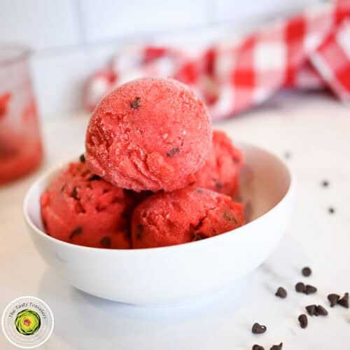 Vegan strawberry ice cream scoops in a white bowl on a white surface.