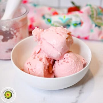 Delicious pink strawberry ice cream scoops in a white bowl on a marble surface.