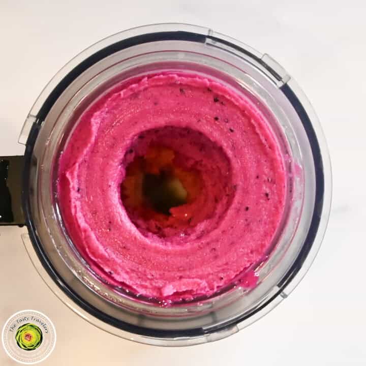 Pink smoothie in a blender with black specks and a circular opening.