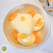 Vanilla ice cream with mango chunks in a white bowl.
