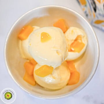 Vanilla ice cream with mango chunks in a white bowl.