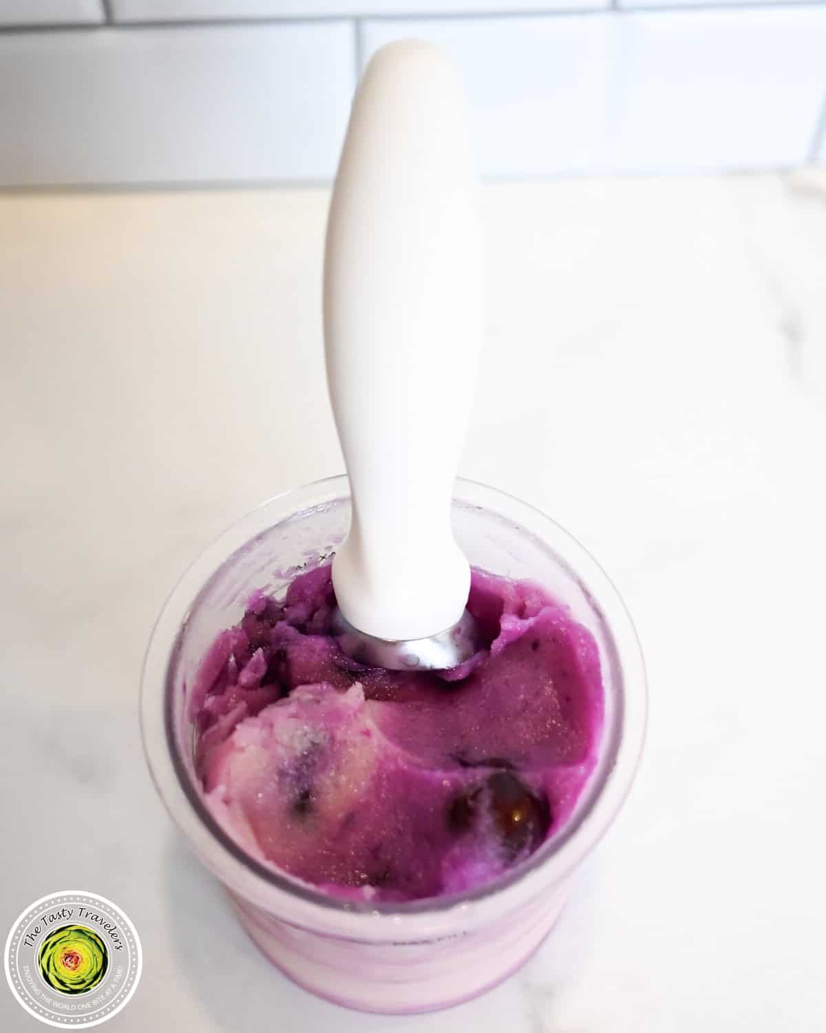 Vibrant purple berry ice cream in a clear cup with a white spoon.
