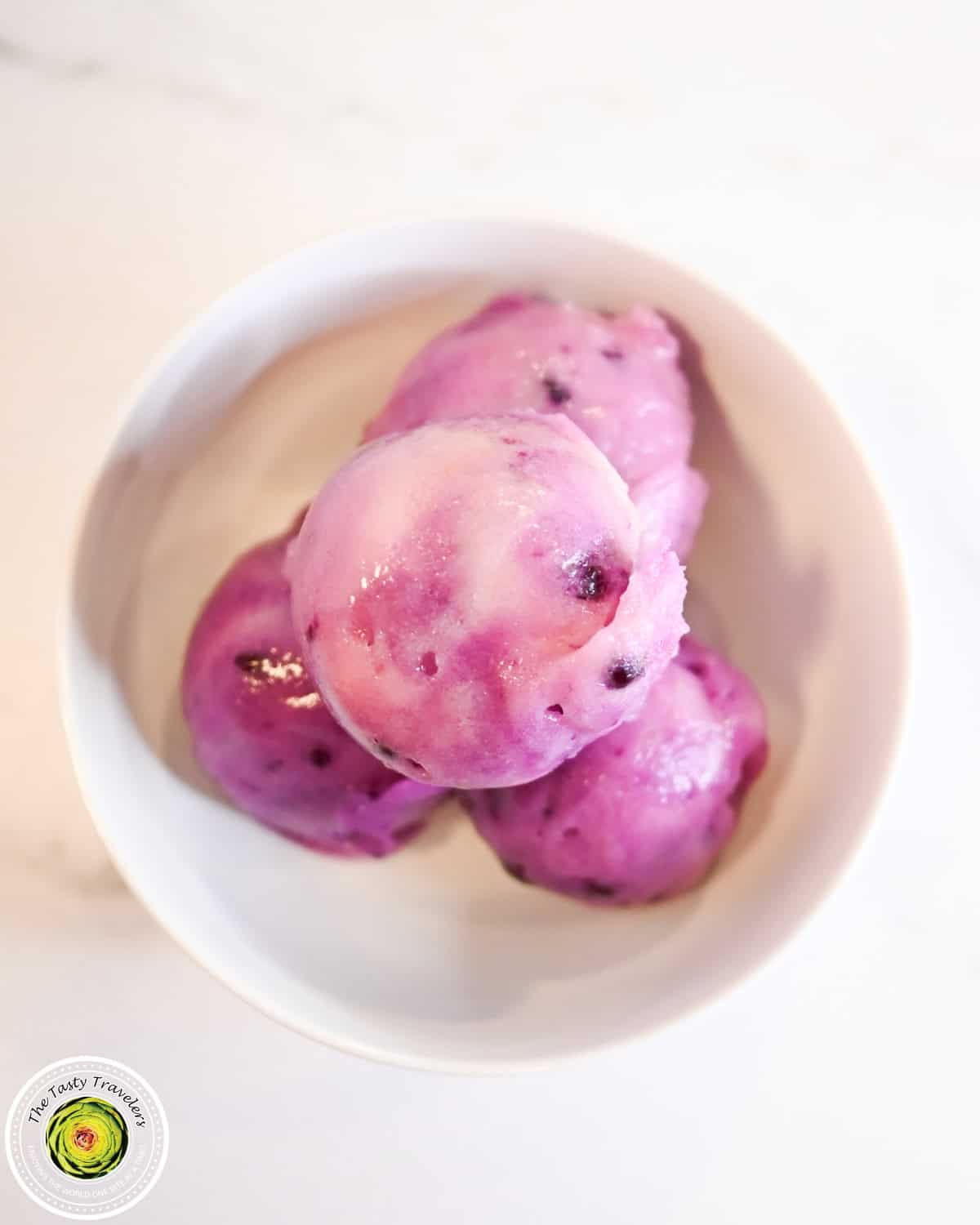 Vibrant purple ice cream scoops in a white bowl on a white surface.
