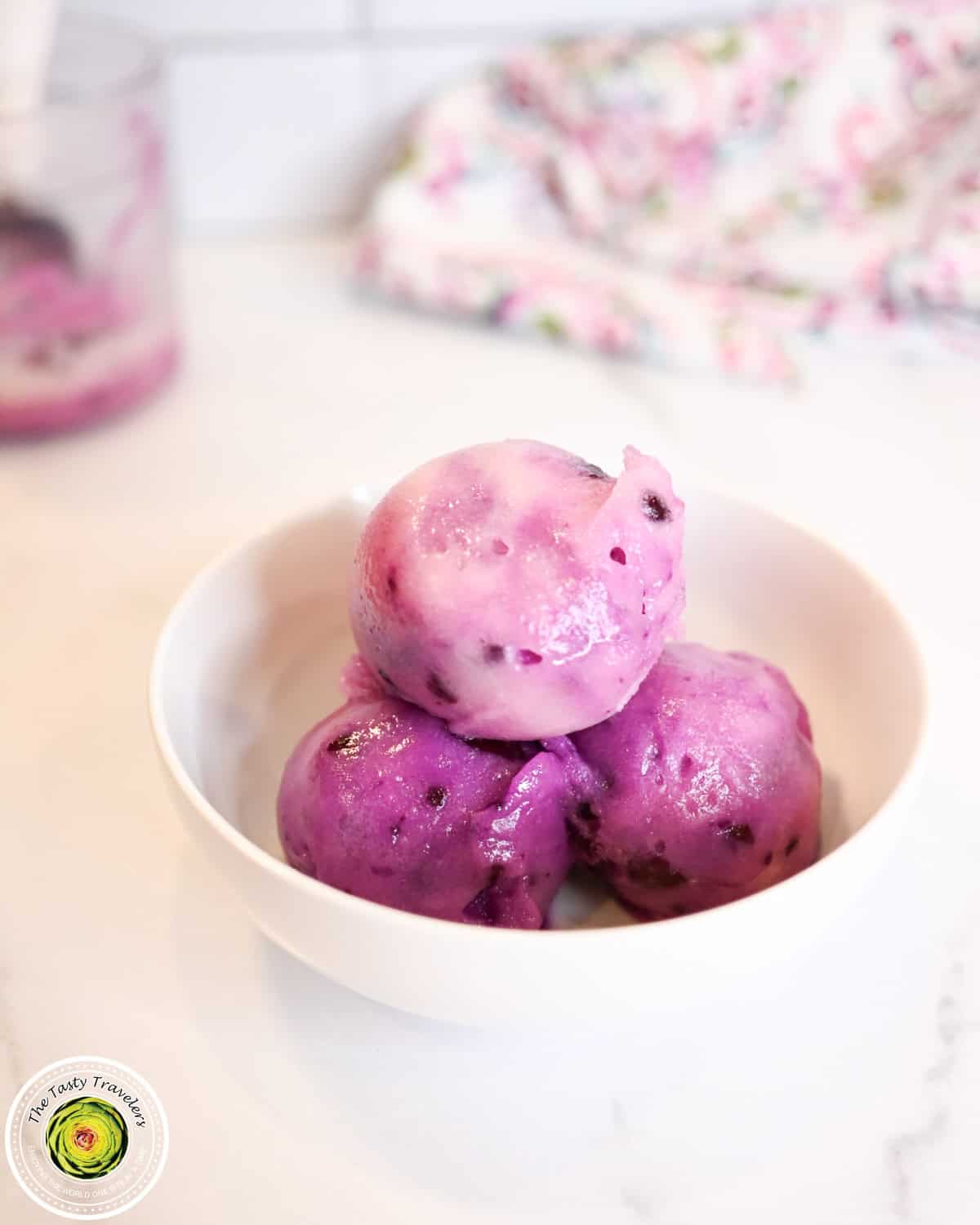 Vibrant purple ice cream scoops in a white bowl on a white surface.
