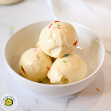 Creamy vanilla ice cream scoops with colorful sprinkles in a white bowl.