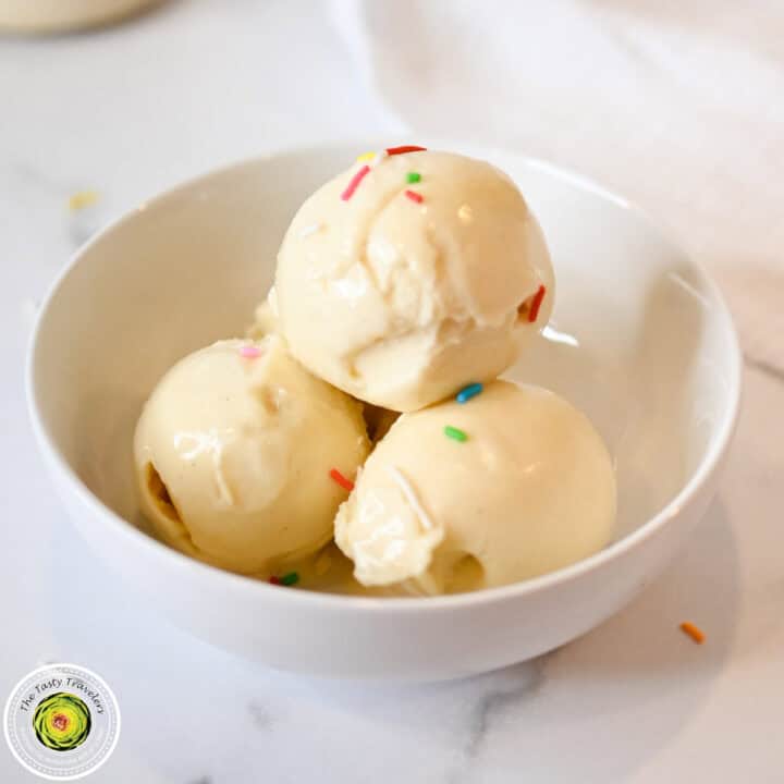 Creamy vanilla ice cream scoops with colorful sprinkles in a white bowl.