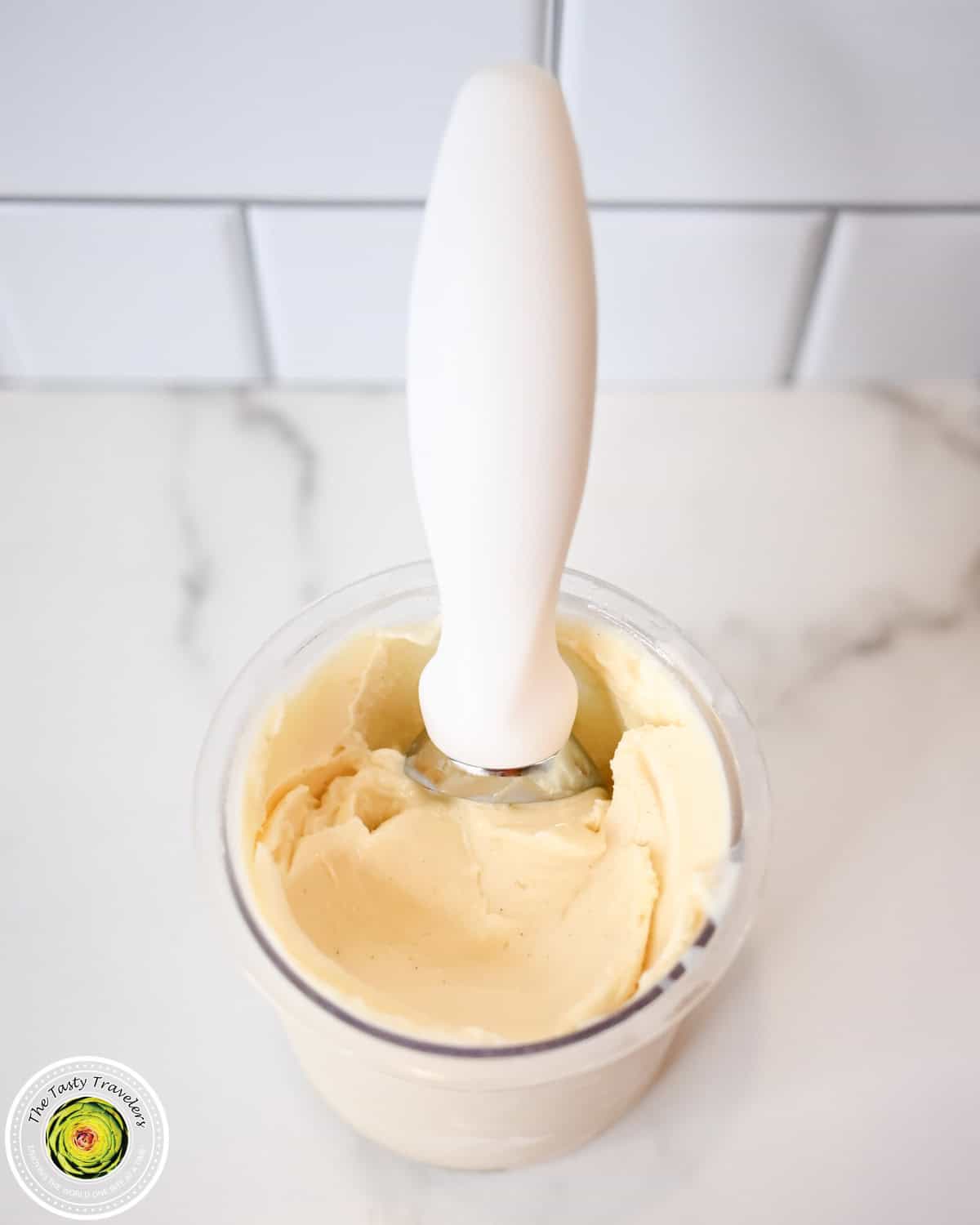 Creamy vanilla ice cream in a clear cup with a white spoon on top.