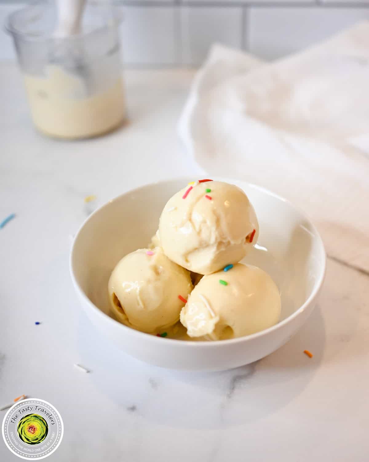Creamy vanilla ice cream scoops with colorful sprinkles in a white bowl.