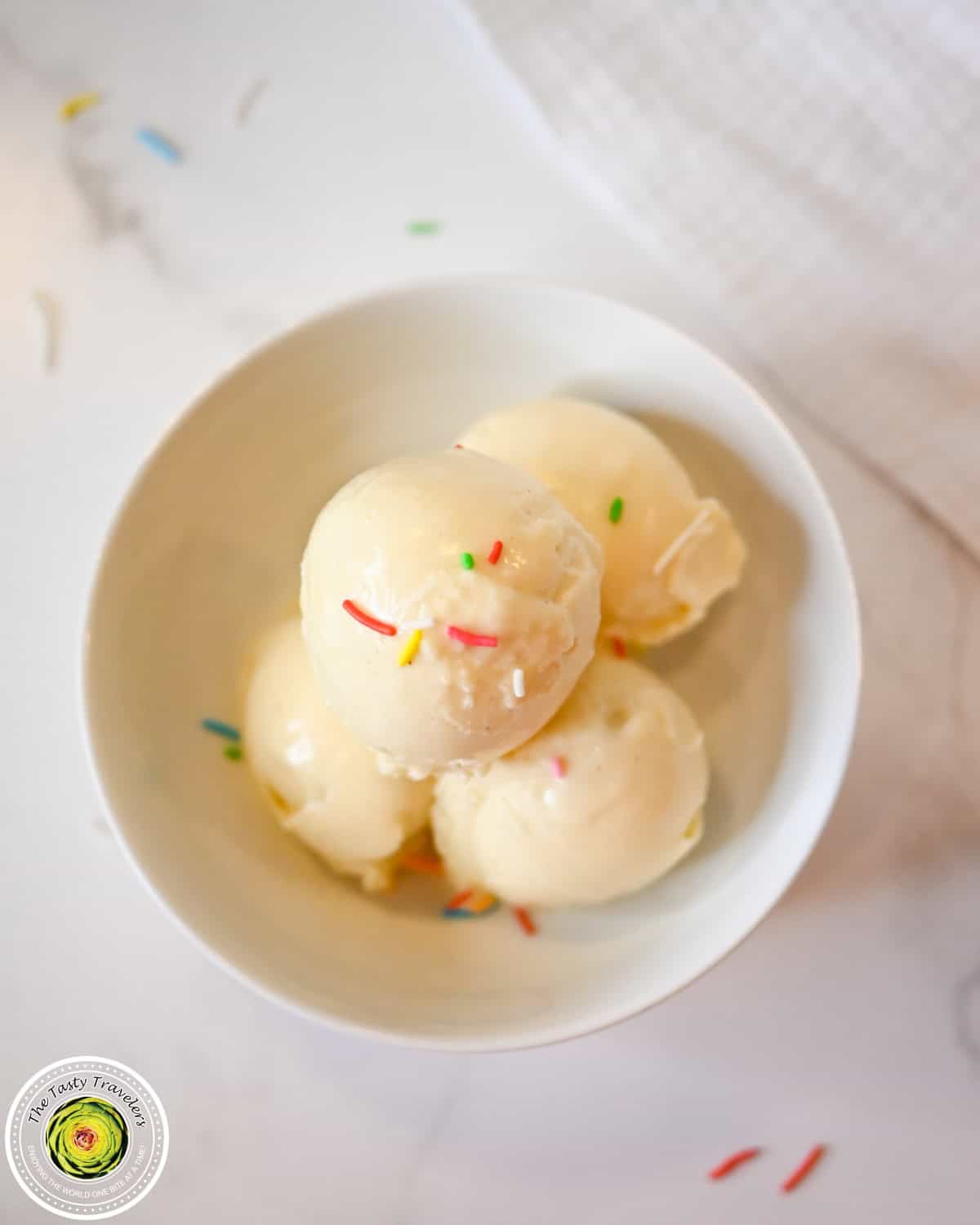 Vanilla ice cream scoops with colorful sprinkles in a white bowl.