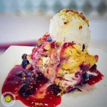 Delicious berry ice cream with fruit topping and sauce on a white plate.
